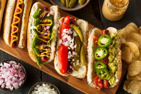Cztery pyszne hot dogi z różnymi dodatkami: musztarda, cebula, pomidor, papryczki i guacamole.