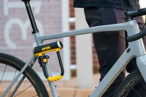 Solidne, żółto-czarne zapięcie rowerowe OnGuard zabezpiecza ramę szarego roweru. Idealne pytanie: jakie zapięcie do roweru wybrać?
