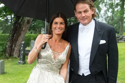 Sian Persson och hennes man, klädda för fest, delar ett paraply i regnet.