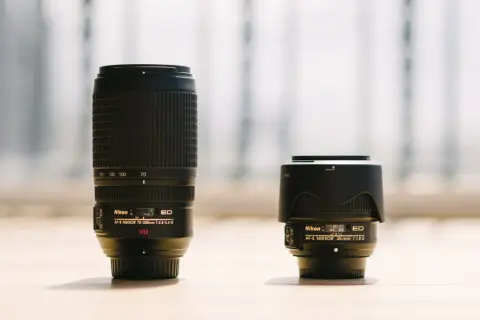 A long telephoto lens stands next to a compact wide-angle lens, showcasing the difference between wide angle vs telephoto perspectives.