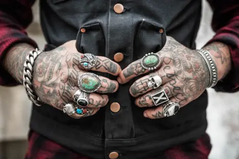 Tätowierter Mann mit vielen Ringen an den Fingern, darunter ein Totenkopf und Türkise.