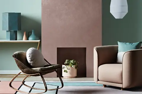 Simulazione abbinamento colori pareti: un salotto con poltrona in vimini, camino rosa e divano beige, su un tappeto geometrico.