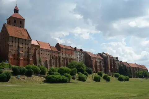 Grudziądz atrakcje: imponująca ceglana twierdza z wieżą i dachem z dachówki, otoczona zielenią i trawnikiem.
