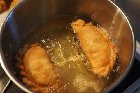 Due calzoni dorati friggono in olio bollente. Si puo friggere con olio d'oliva per un sapore autentico.
