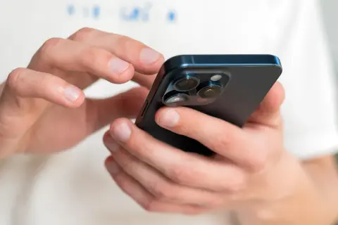 Dłonie trzymające ciemny iPhone, na którym można sprawdzić numer IMEI.