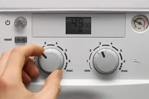 Ręka kręci pokrętłem pieca gazowego dwufunkcyjnego, ustawiając temperaturę. Wyświetlacz pokazuje 49°C.