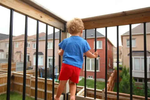 Kleines Kind auf einem sicheren Balkon, das neugierig die Nachbarschaft erkundet.