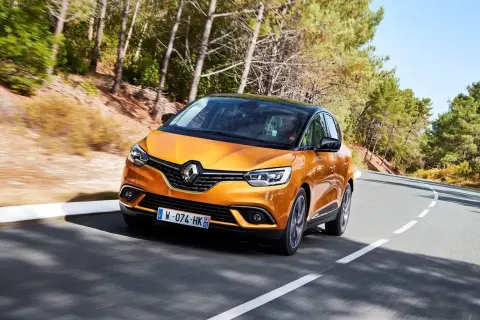 Pomarańczowy Renault Scenic 4 na krętej drodze. Choć wygląda świetnie, warto znać jego potencjalne wady przed zakupem.