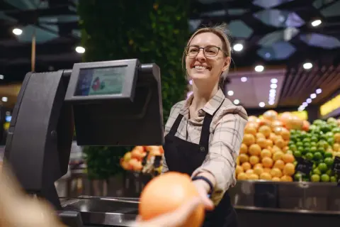 Uśmiechnięta kasjerka podaje pomarańczę. Czy to jeden z ostatnich takich zawodów, które znikną przez automatyzację?