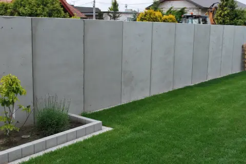 Nowy, wysoki betonowy płot dzieli działki, symbolizując konflikt z sąsiadem o ogrodzenie.
