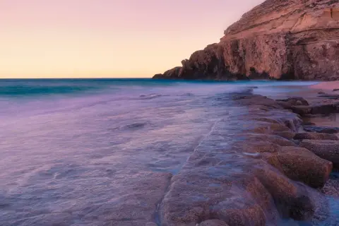 El mar acaricia las rocas de la cala el corral carboneras al atardecer, creando un paisaje sereno y etéreo.