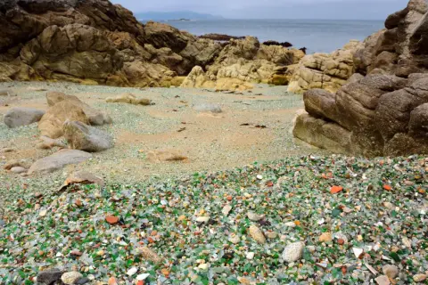 La praia dos cristais, una playa de guijarros de vidrio pulido por el mar, rodeada de rocas y con el océano al fondo.
