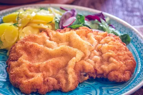 Ein knuspriges Wiener Schnitzel mit Kartoffelsalat und Zitrone auf einem blauen Teller.