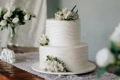 Elegancki tort komunijny, idealny na 20 osób. Białe kwiaty zdobią dwupoziomowe ciasto.