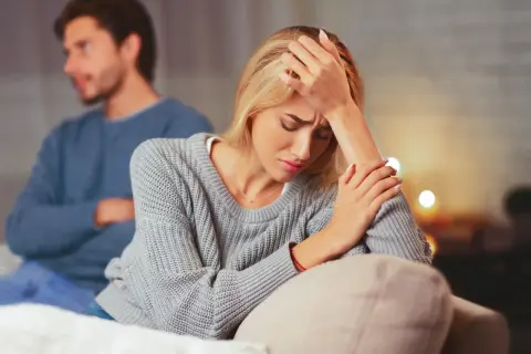 Una mujer angustiada en primer plano, con un hombre de espaldas en el fondo. La escena evoca la confusión y el dolor que a veces acompañan a **que es la limerencia**.