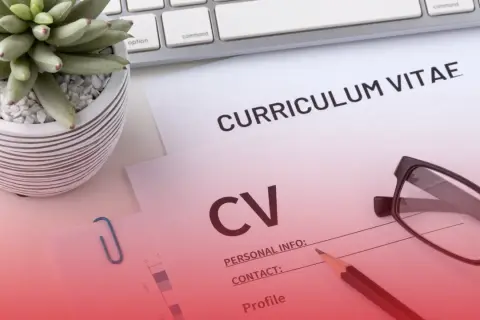Na biurku leżą dokumenty CV, okulary i ołówek. Roślina w doniczce i klawiatura dopełniają scenę.