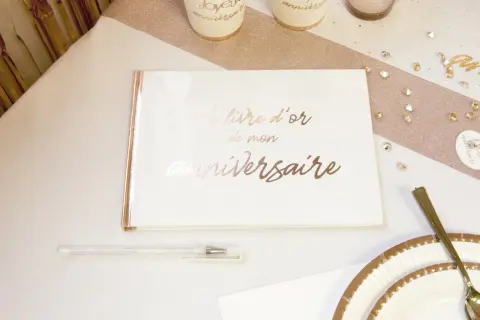 Un livre d'or de mon anniversaire, prêt à recueillir les vœux les plus doux. Un stylo blanc et des décorations dorées complètent la scène festive.