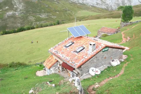 Refugio en Picos de Europa, con paneles solares en el tejado. Vacas pastan en la ladera verde.