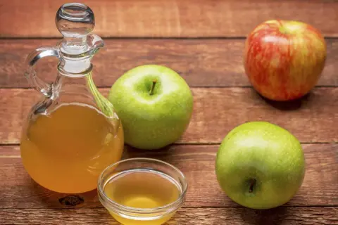 Apfelessig in einer Karaffe und Schale, daneben Äpfel. Vielseitige Apfelessig Anwendung für Küche und Gesundheit.