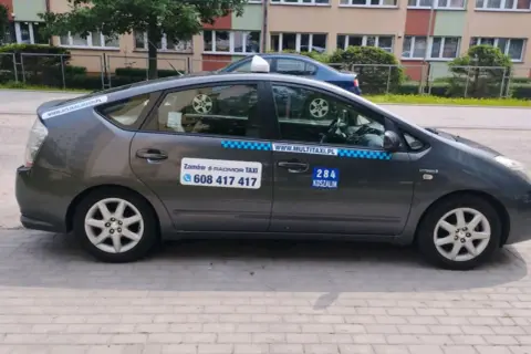 Szary hybrydowy Prius z napisem "284 KOSZALIN" i numerem telefonu do zamówienia taksówki.