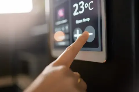 Dedo tocando el botón de menos en un termostato digital que muestra 23°C. Aprende como programar un termostato digital.