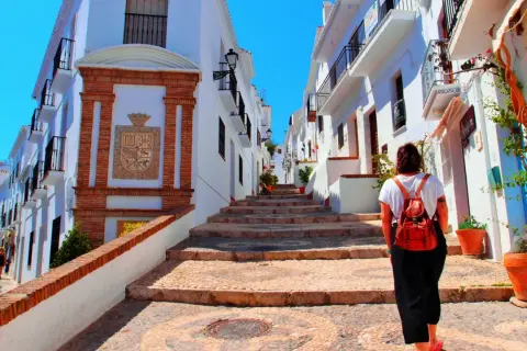 Una mujer con mochila sube escaleras empedradas en un pintoresco pueblo blanco, quizás el pueblo mas bonito de Andalucia.