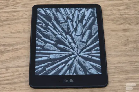 Un Kindle, une liseuse électronique affichant une image abstraite de plumes d'encre, sur un fond en bois.