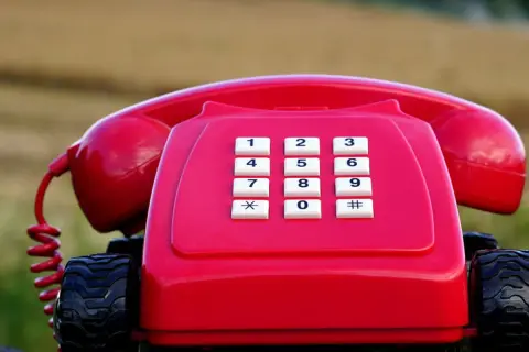 Czerwony telefon stacjonarny na kółkach, jakby gotowy do podróży po najtańszy abonament.