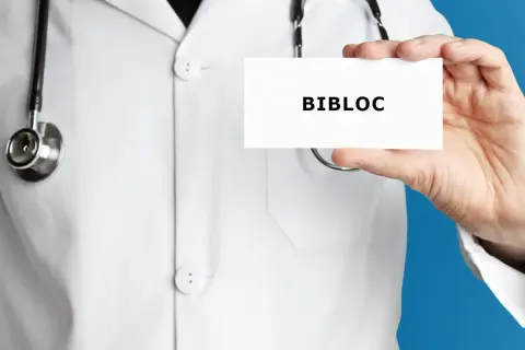 Lekarz w białym kitlu trzyma wizytówkę z napisem BIBLOC. Stetoskop wisi na jego szyi.
