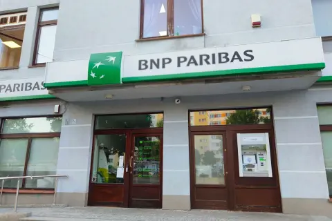 Wejście do placówki banku BNP Paribas z zielonym logo i napisem. Obok drzwi znajduje się bankomat.