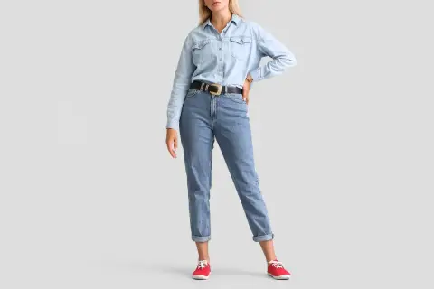 Modelka w jasnych jeansach z podwiniętymi nogawkami i jeansowej koszuli. Idealne jeansy dla niskiej osoby, które optycznie wydłużają nogi.