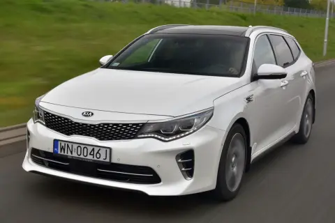 Biała Kia Optima w wersji kombi na drodze. Wiele pozytywnych kia optima opinie potwierdza jej wszechstronność.