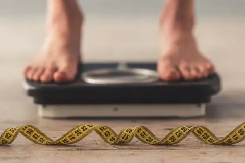 Pieds sur une balance, ruban à mesurer enroulé au premier plan. La question "pourquoi je ne perds pas de poids" résonne.