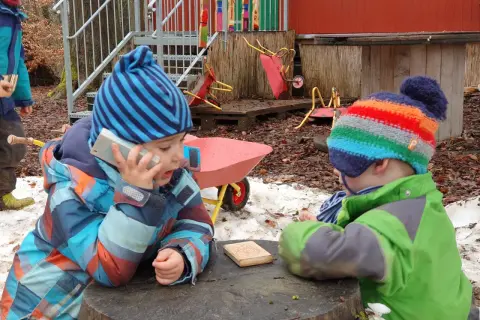 Zwei Kinder im Wald Kindergarten spielen mit einem Spielzeugtelefon und einem Holzklotz.