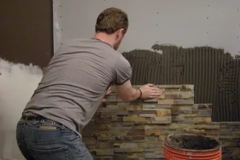 Mężczyzna układa kamień dekoracyjny betonowy. Do cięcia takiego materiału używa się specjalistycznych narzędzi.