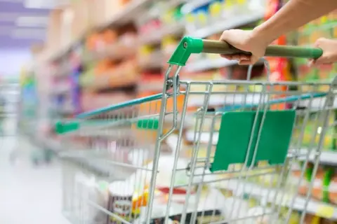 Ręka pcha wózek sklepowy w alejkach sklepu spożywczego, tworząc obraz dynamicznego doświadczenia w branży retail.