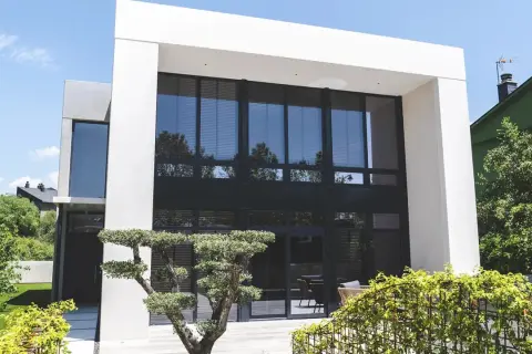 Moderna casa con fachada gris y beige, grandes ventanales y jardín cuidado.
