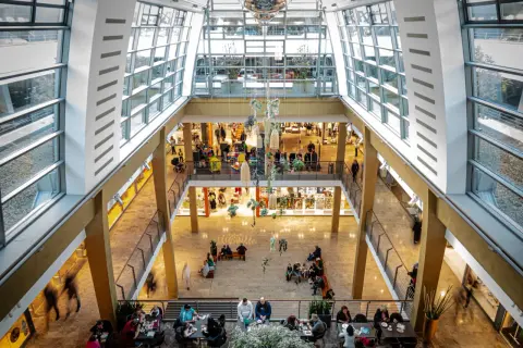 Blick in ein helles Einkaufszentrum in Bergisch Gladbach mit vielen Besuchern, Geschäften und Sitzbereichen.
