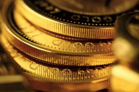 Zbliżenie na stos złotych monet z widocznym napisem "GOLD".