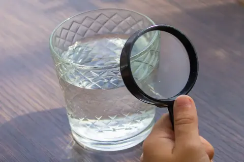 Une main tient une loupe pour analyser l'eau d'un puits dans un verre.