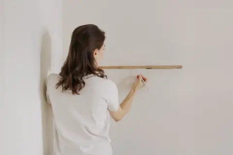 Frau misst die Wand, um zu entscheiden, wo anfangen mit dem Tapezieren.