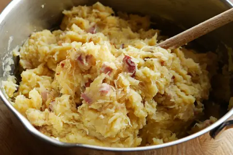 Panczkraut w garnku, gotowy do podania. Drewniana łyżka miesza ziemniaczaną masę z kawałkami boczku.