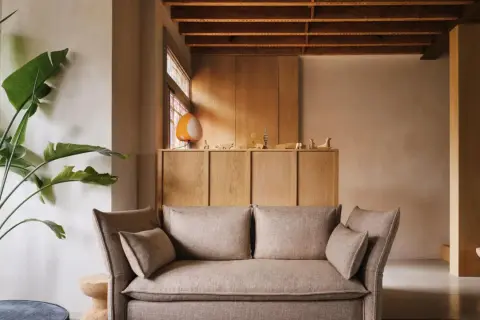 Gemütliches Wohnzimmer mit beigem Sofa, großer Zimmerpflanze und einem Schrank aus hellem Holz, der zum holz streichen einlädt.