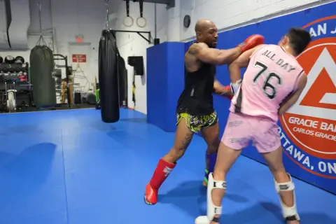 Two fighters practice boxing head movement drills in a gym. One throws a punch while the other dodges.