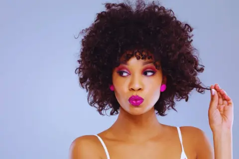 Mujer con rizos chicos y maquillaje vibrante, jugando con un mechón de su cabello.