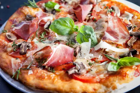 Pyszna pizza parma z szynką, pieczarkami, pomidorami i bazylią, posypana parmezanem.
