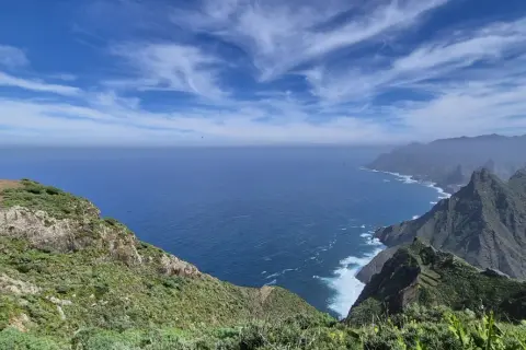 Vista del Roque de Tábarno, un promontorio verde y rocoso que se adentra en el mar azul bajo un cielo nublado.