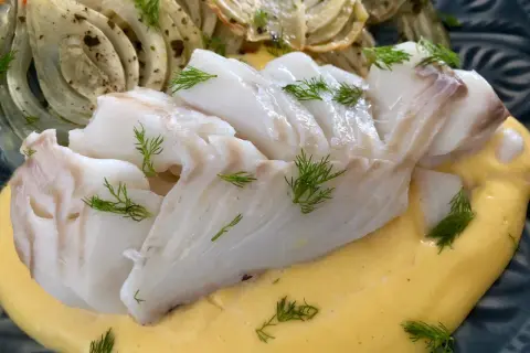 Vit fisk serveras med krämig sås och ugnsbakad fänkål, garnerad med dill.