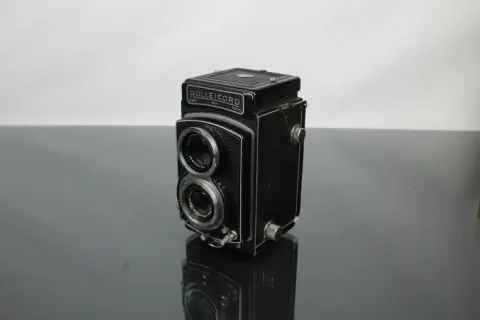 A vintage Rolleicord camera sits on a reflective surface, its twin lenses and classic design hinting at a rich photographic history.