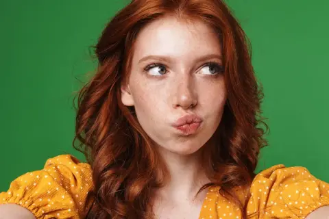 A young woman with fiery red hair, often symbolizing passion and uniqueness, puckers her lips against a vibrant green backdrop.